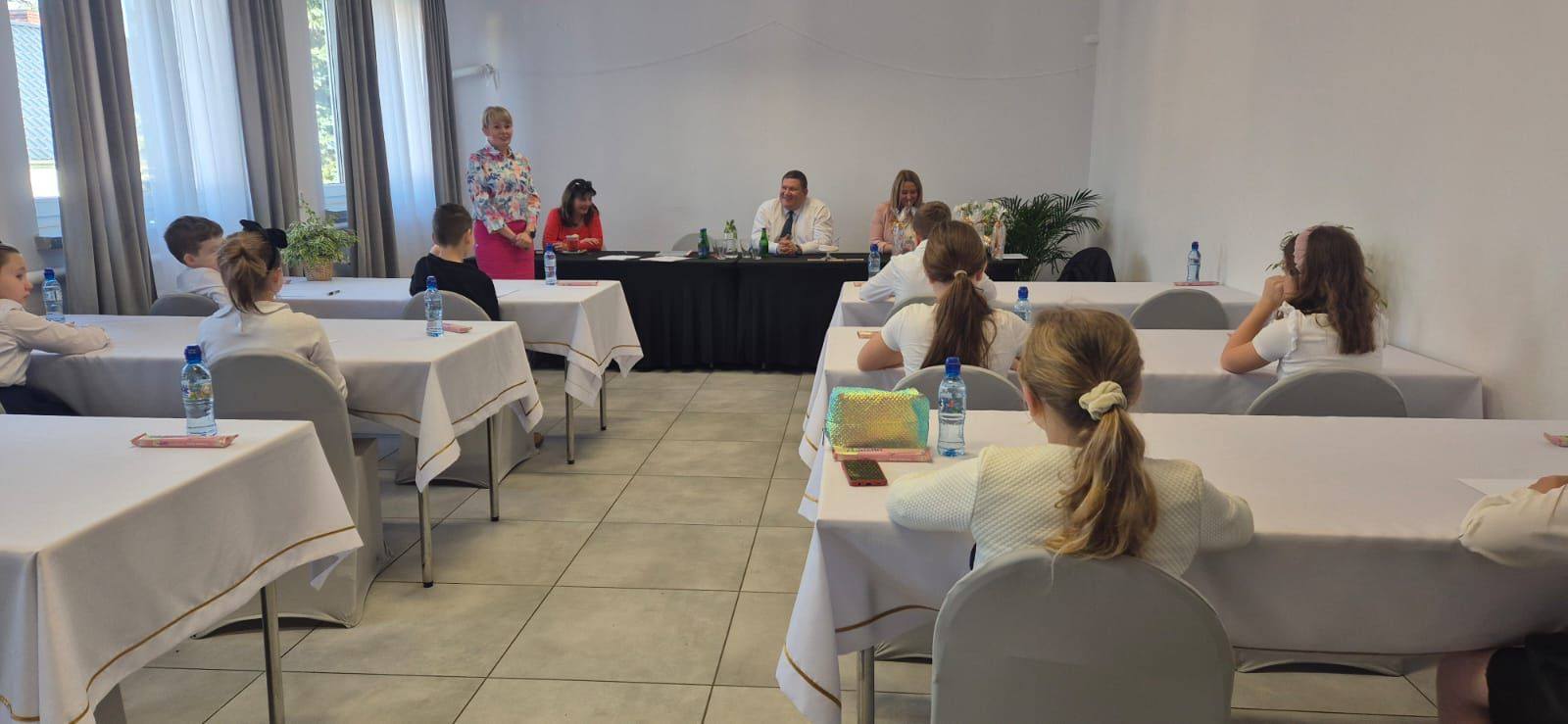 Dzieci siedzą na krzesłach i wychowawcy